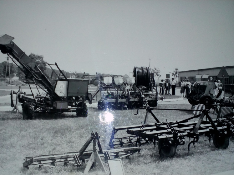 Czarno-białe zdjęcie. Maszyny rolnicze stoją na trawie na terenie targów.