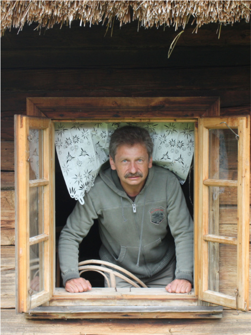 Stanisław Zabarski pozuje do obiektywu wyglądając przez okno drewnianej chaty.
