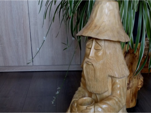 Drewniana figurka przedstawiająca siedzącą postać z brodą oraz w kapeluszu. 