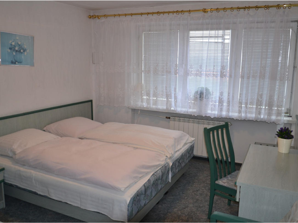 Wnętrze apartamentu w Sielinku Wnętrze apartamentu. Duże łóżko stoi pod ścianą. Przed nim stoi biurko i krzesło. W tle są okna.